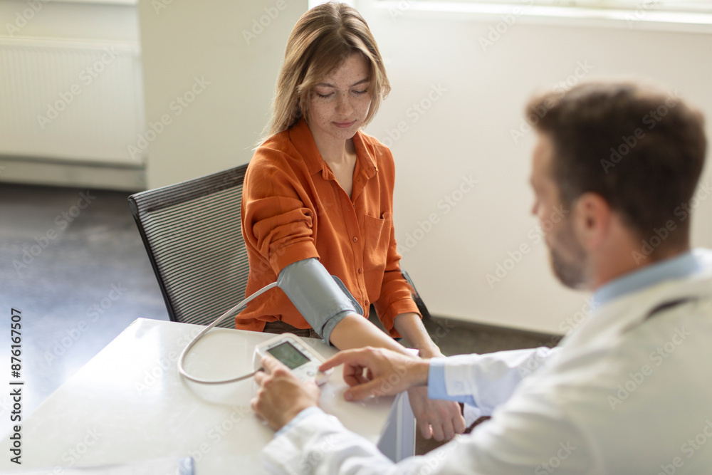Fototapeta premium Man doctor measuring blood pressure of sick young woman patient with tonometer during an examination in the clinic
