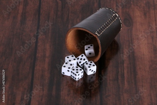 Leather dice cup lies on the wooden table and six white dice fall out

