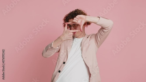 Caucasian man photographer gesturing picture frame with hands, looks through fingers and focusing on interesting moment, imitating zoom and cropping nice image. Young guy isolated on pink background