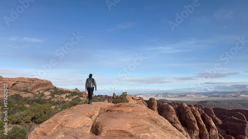 Female hiker on a high, narrow sandstone rock fin formation with views of the desert landscape. Enjoying the view on the Devils Garden Trail in Arches National Park, Utah - USA