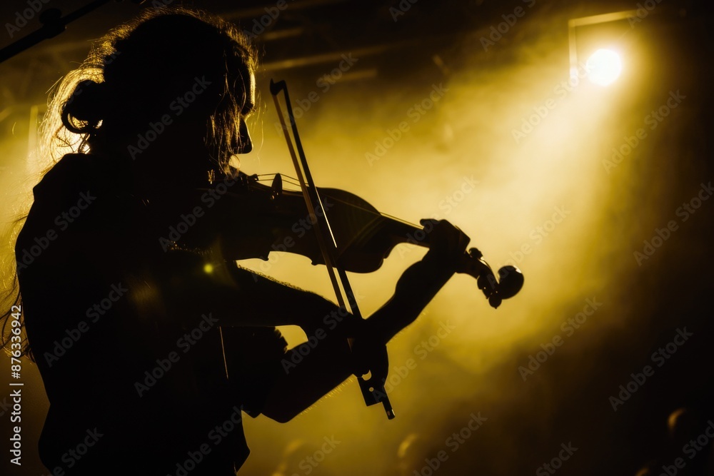 Fototapeta premium A silhouetted violinist performs on stage under the warm glow of stage lights, their passion and dedication visible in their focused posture