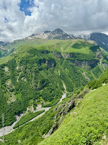 Panoramic view of green lush Caucasus mountains with snow peaks and tiny river in Kazbegi, Georgia photo