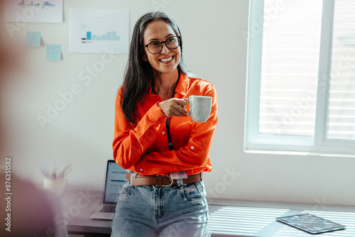 Woman in orange shirt holding coffee cup and smiling in a bright office environment