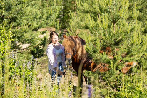 Woman with Icelandic horse between pines at summer evening