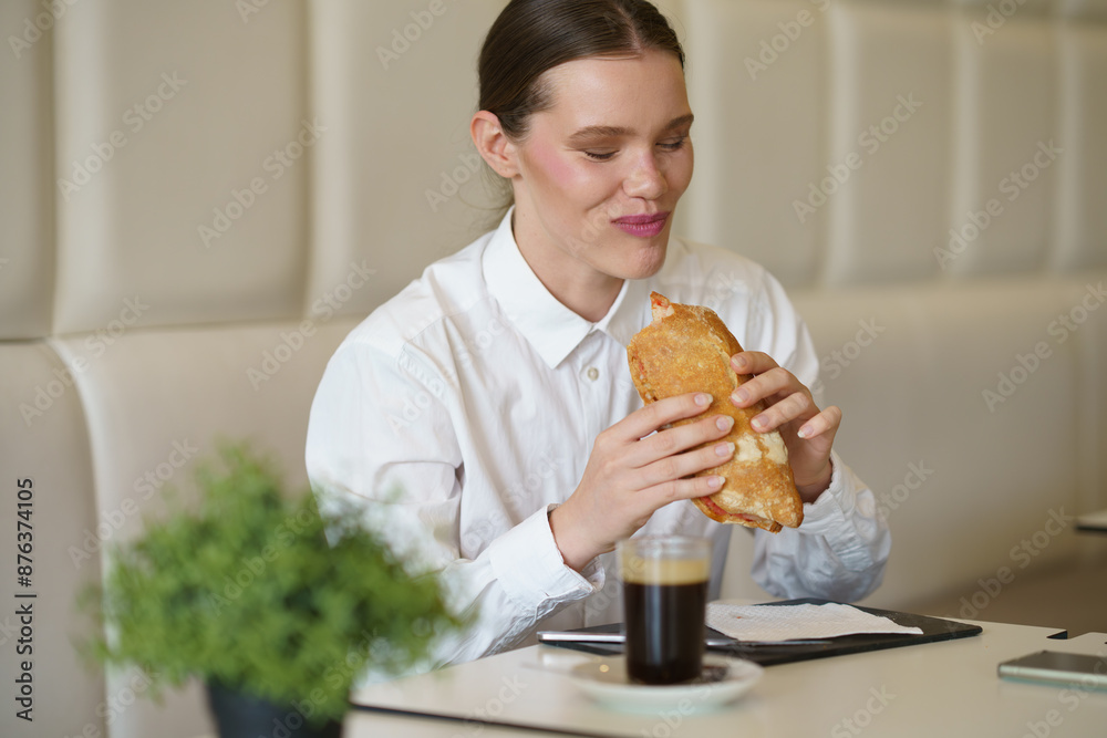 Smiling businesswoman eating a sandwich in a modern coffee shop Smiling businesswoman eating a sandwich in a modern coffee shop