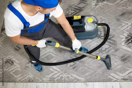 A top view image featuring a cleaning company worker in a specialized uniform and protective gear, including gloves and overshoes, utilizing a high-quality vacuum cleaner for deep cleaning a carpet.