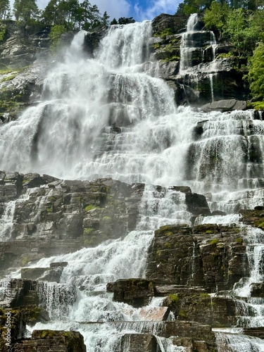 A waterfall is surrounded by rocks and trees on a beautiful sunny day