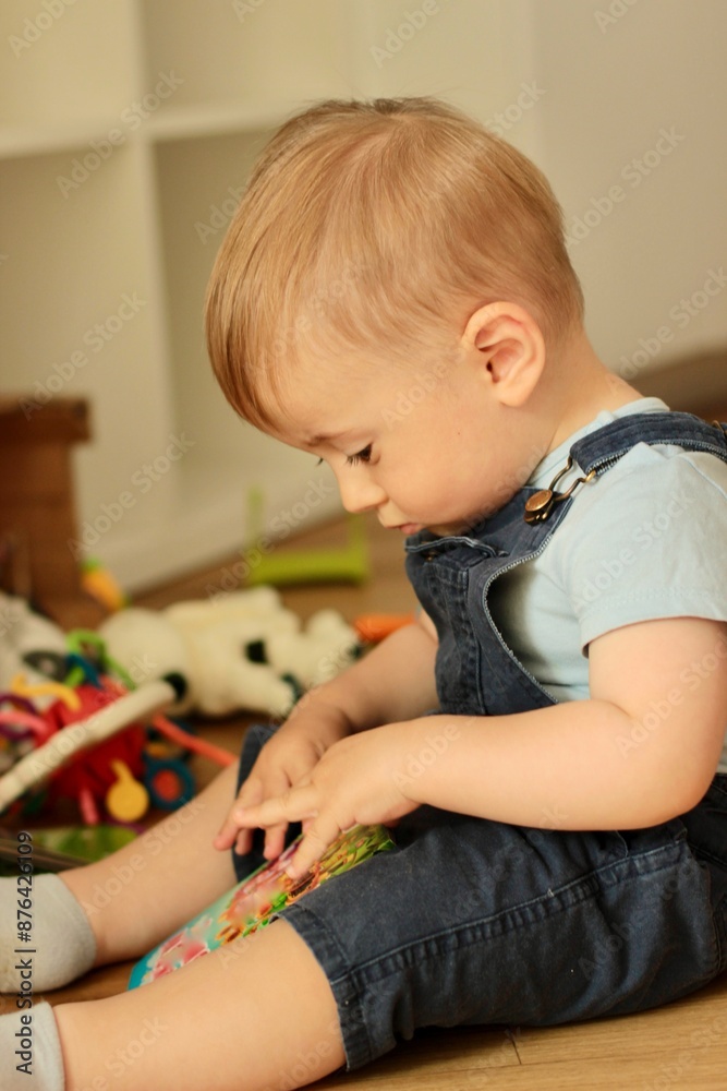A small child sits among toys and looks at children's books with interest A small child sits among toys and looks at children's books with interest