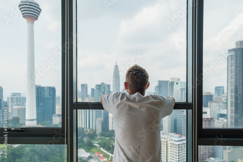 Canvas Print Rear view of thoughtful man in modern apartment looking at panoramic window with Kuala Lumpur city view