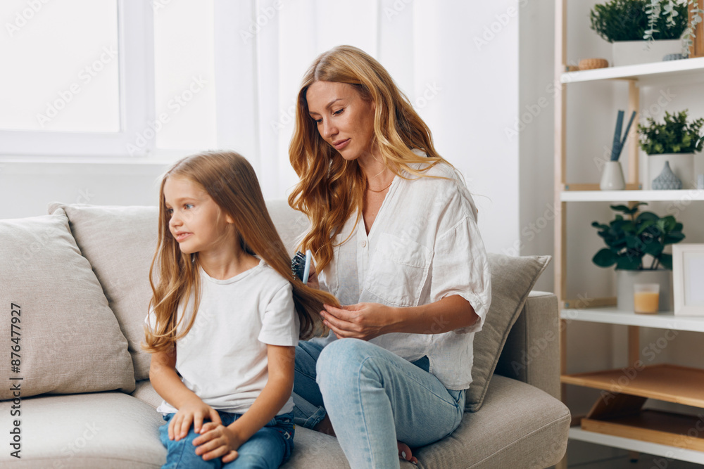 Obraz premium Mother and daughter sharing quality time on a cozy couch in front of a wooden bookshelf in a warm living room