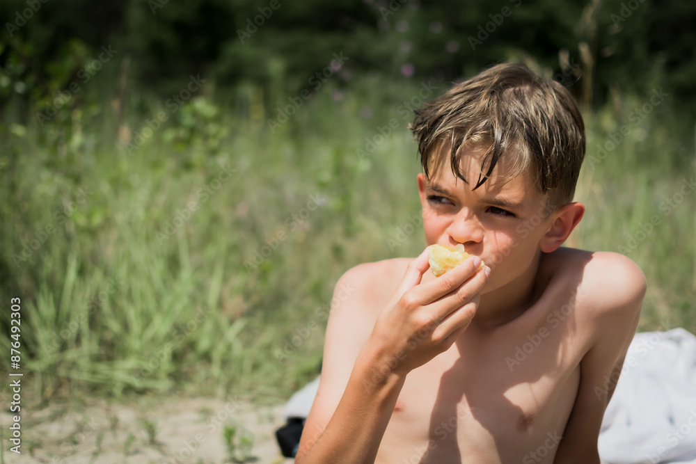Fototapeta premium A little boy eats food on the beach after swimming