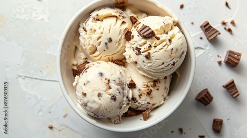 A top view of creamy peanut butter cup ice cream scoops in a white bowl, surrounded by chocolate pieces. Perfect for dessert, sweets, and indulgence concepts