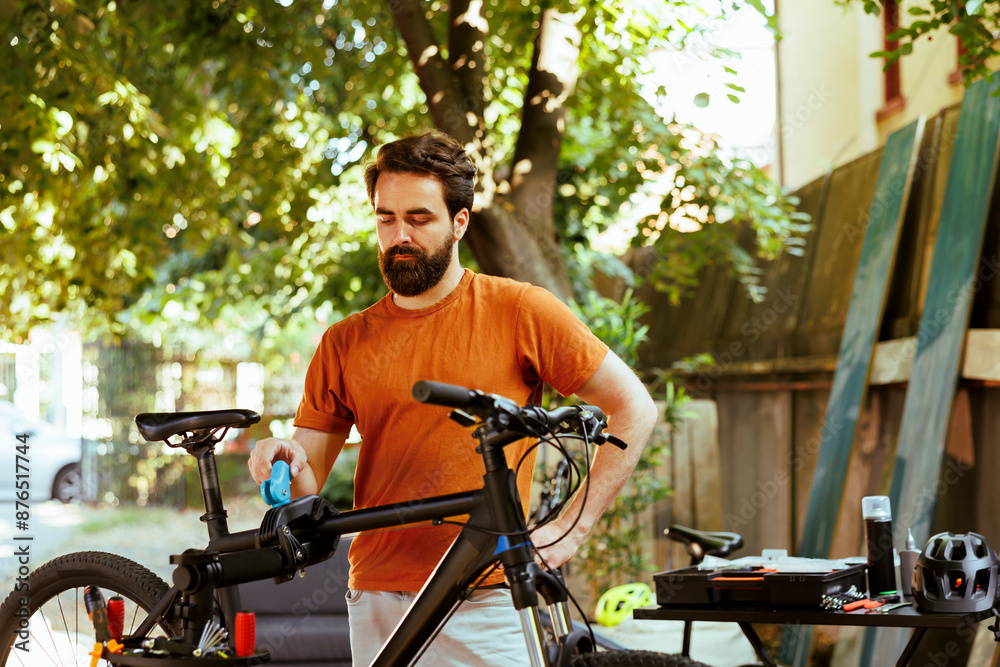 Healthy committed caucasian man clamping bike frame to repair-stand for safe outdoor maintenance. Sports-loving male cyclist realigning and adjusting bicycle for servicing in yard. Healthy committed caucasian man clamping bike frame to repair-stand for safe outdoor maintenance. Sports-loving male cyclist realigning and adjusting bicycle for servicing in yard.