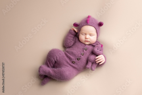 Little adorable newborn baby girl sleeping in a hat with dragon ears. Neutral background. Studio shot of a ten-day-old newborn baby. Beginning of life. Fairy tale. Dragon toy © Svetlana