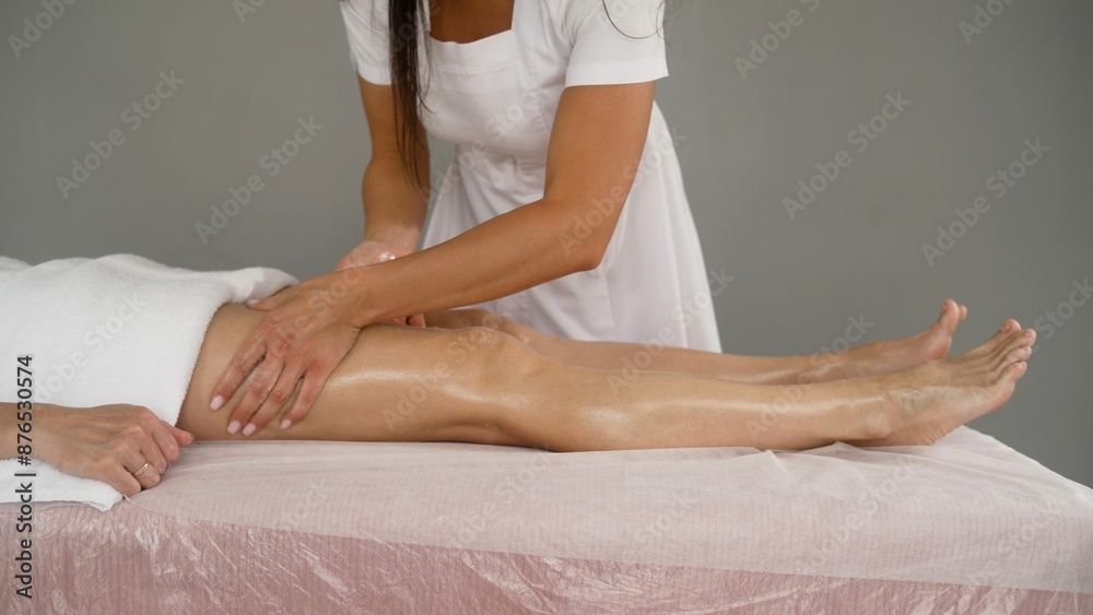 Fototapeta premium The masseuse sprinkles the solution on the client's leg. Cosmetic procedure for the body and legs for a woman. The cosmetologist applies a scrub solution to the patient s leg and rubs it.