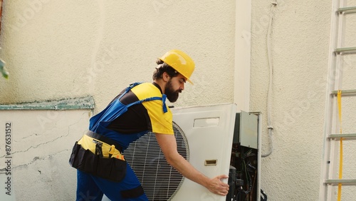 Expert technician contracted to repair broken air conditioner, dismantling condenser front coil panel to check faulty blower fan. Wireman opening hvac system to check for bad wiring