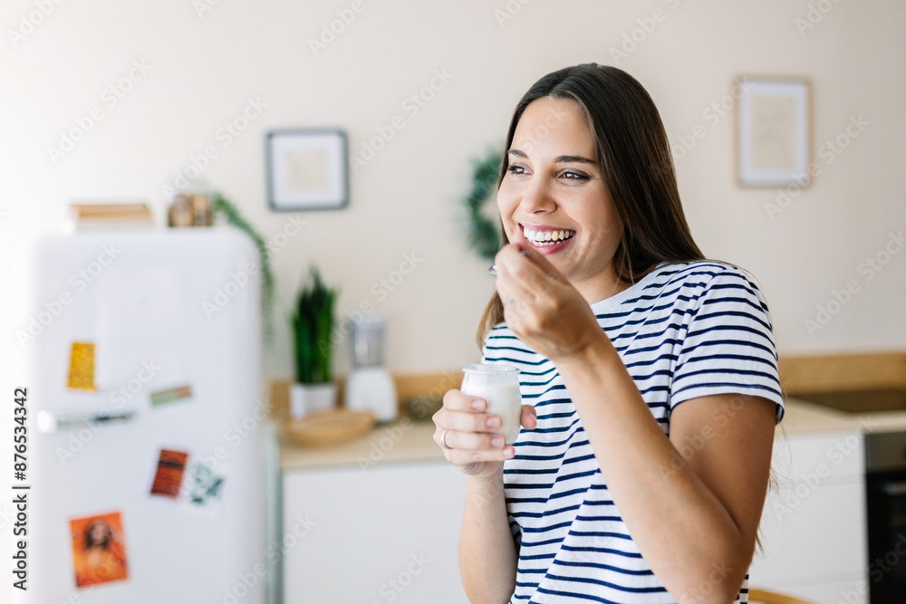 Happy young woman eating a yogurt for breakfast at home. Healthy lifestyle concept Happy young woman eating a yogurt for breakfast at home. Healthy lifestyle concept