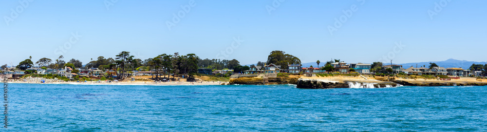 Scenic panoramic view of Santa Cruz shoreline as seen from the water, featuring sandy beaches, residential homes, and tall trees against a bright, clear sky Scenic panoramic view of Santa Cruz shoreline as seen from the water, featuring sandy beaches, residential homes, and tall trees against a bright, clear sky