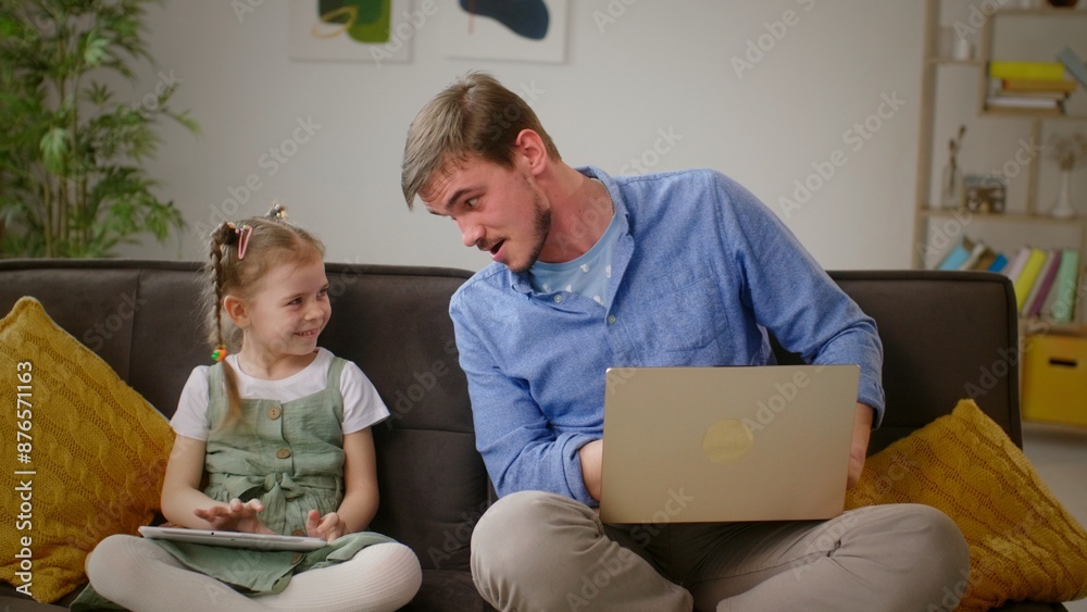 Obraz premium Shared Smiles: Father Shows Humorous Images to Daughter on Sofa
