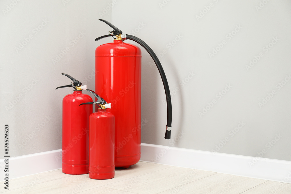 Obraz premium Fire extinguishers on floor near light grey wall, space for text