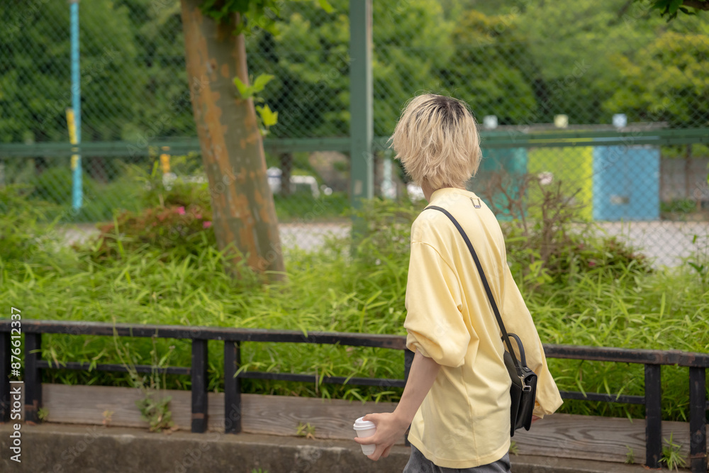 Fototapeta premium In early summer, a Japanese man in his twenties wearing yellow clothes, walking and strolling through Yoyogi Park, Shibuya, Tokyo, during the day.