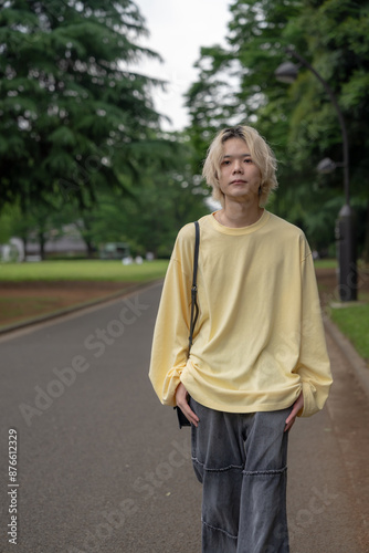 In early summer, a Japanese man in his twenties wearing yellow clothes, walking and strolling through Yoyogi Park, Shibuya, Tokyo, during the day.