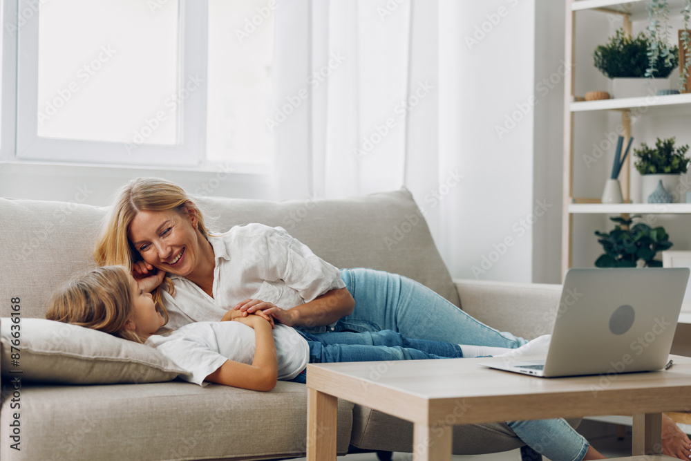 Mother and child bonding on the couch, watching something on a laptop, her hand gently resting on his head Mother and child bonding on the couch, watching something on a laptop, her hand gently resting on his head