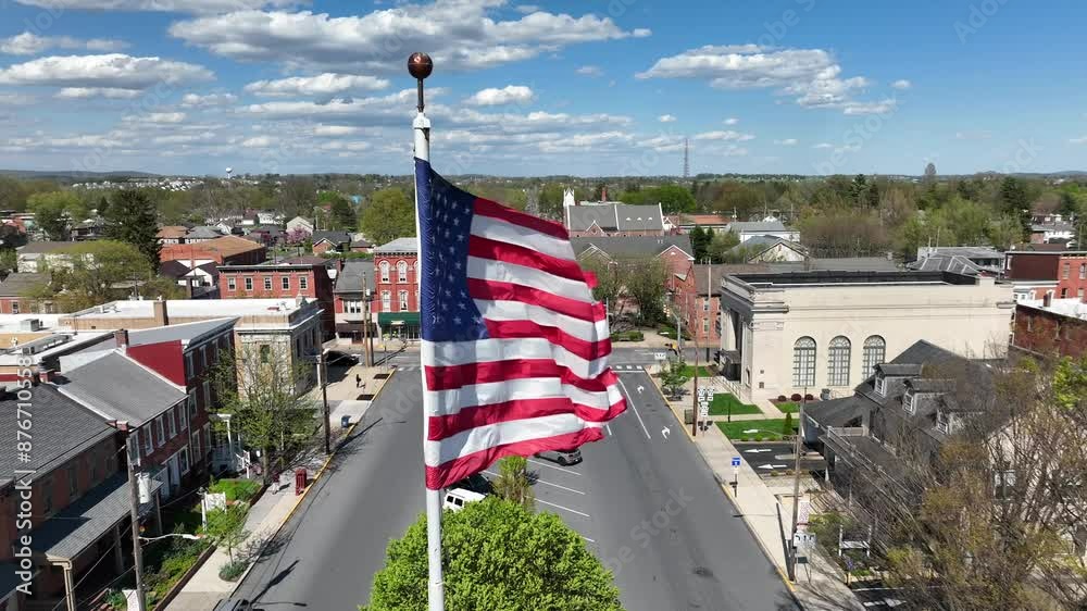 Patriotic american flag on city square of small town during sunny day.  Historic Buildings of american city. Aerial close up shot.