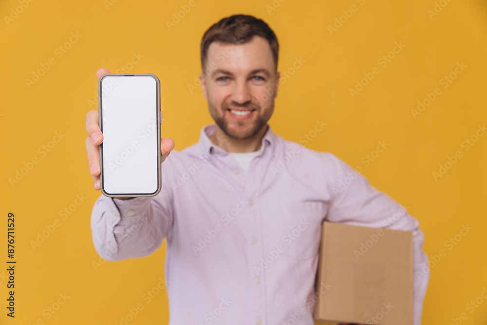 Handsome unshaven man wear shirt casual clothes hold stack cardboard boxes use blank screen mobile cell phone isolated on yellow background studio portrait Handsome unshaven man wear shirt casual clothes hold stack cardboard boxes use blank screen mobile cell phone isolated on yellow background studio portrait