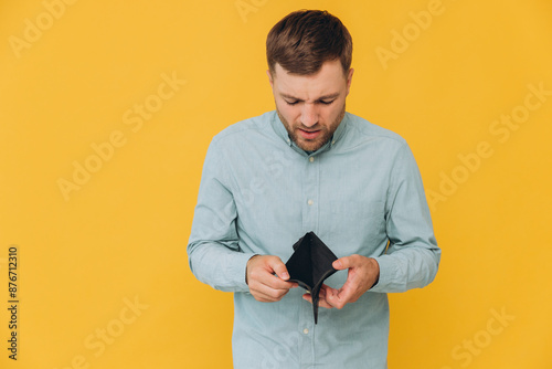 I'm Broke. Portrait of sad unshaven male bankrupt showing his empty wallet looking at camera. Upset man standing isolated over yellow studio background. Poverty Concept. Lack of money