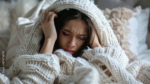 Close up of woman feeling unwell at home, lying in bed under white blankets and frowning, touching head, has headache, migraine,Image of girl feeling sickness.