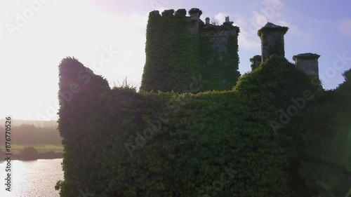 Slow aerial pan captures Menlo Castle with ivy-covered top against the sun, revealing River Corrib. photo