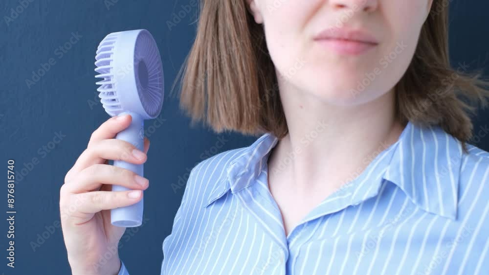 Female hand holding mini fan on blue background close-up. Female hand holding mini fan on blue background close-up.