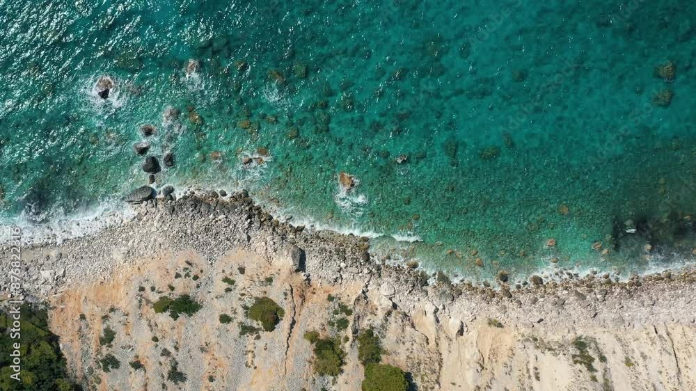 An aerial view captures the stunning interface between a turquoise sea and the rugged beauty of a rocky coastline.