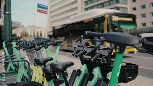 A row of green electric scooters parked in Lisbon, Portugal with a bus in the background. Urban city transportation and eco-friendly travel concept. Green Electric Scooters And Bikes Parked