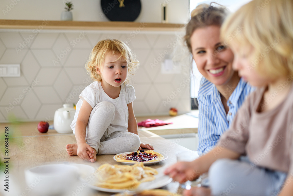 Family eating pancakes together, morning in the kitchen. Mom and children spending weekend day indoors. Family eating pancakes together, morning in the kitchen. Mom and children spending weekend day indoors.