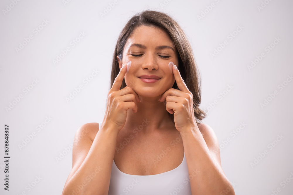 Portrait of adult woman who is applying skin cream on her face. Portrait of adult woman who is applying skin cream on her face.