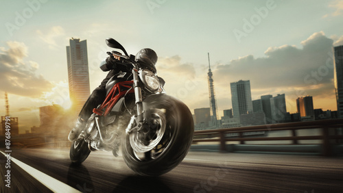 Принти на полотні Motorcyclist speeds along city road at sunset, leaning into the curve with skyscrapers in the background