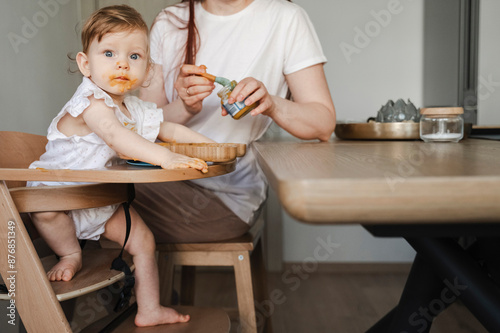 Mother feeding daughter sitting in high chair at home