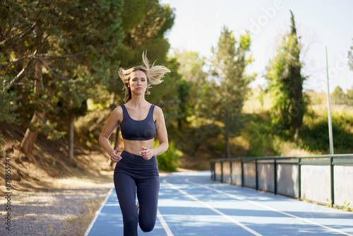 Athletic blond hair woman running on track at field photo