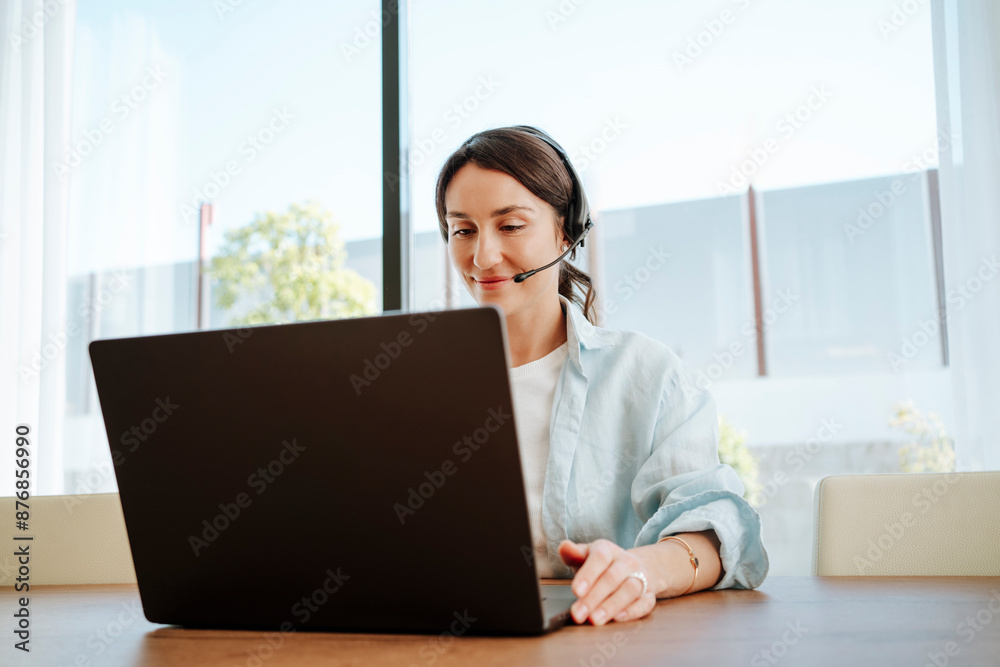 Smiling customer service representative with headset and laptop at table working from home Smiling customer service representative with headset and laptop at table working from home