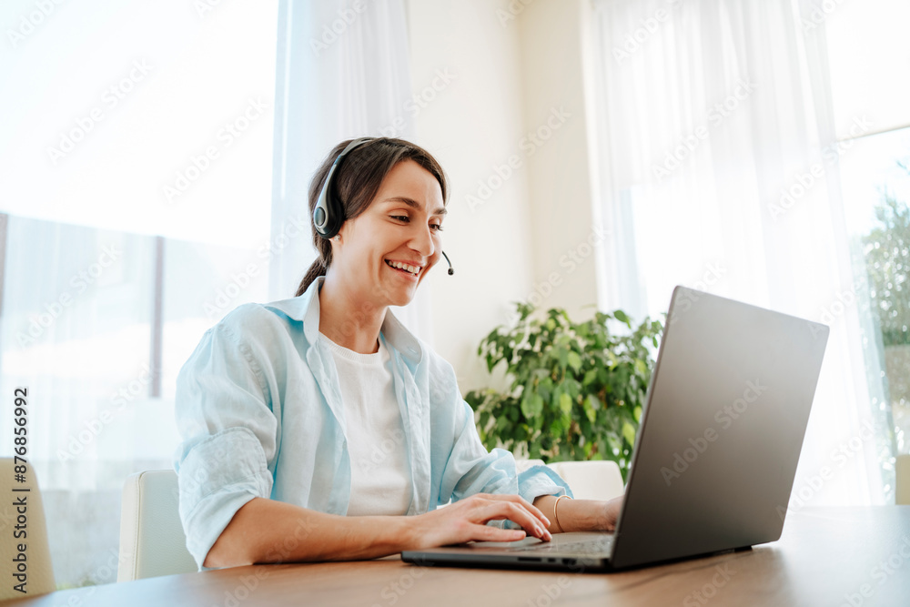 Happy customer service representative with headset using laptop at table working from home Happy customer service representative with headset using laptop at table working from home