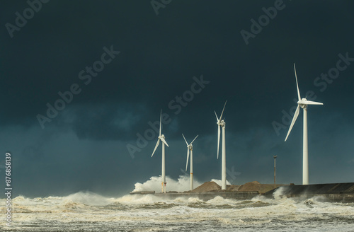 Waves breaking near wind turbines on coastline under cloudy sky photo