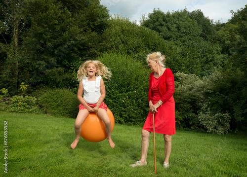 Granddaughter having fun with grandmother standing on grass in garden