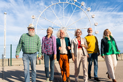 Retired men and women walking side by side in front of Ferris wheel on sunny day