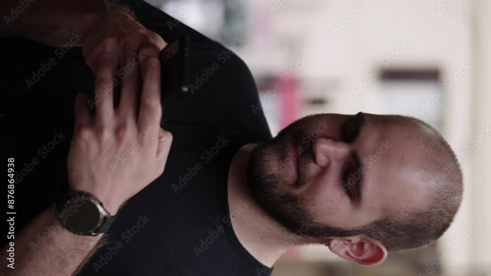 A young man with light beard stubble sends an SMS on his smartphone in a vertical clip, appearing focused and engaged in his digital communication A young man with light beard stubble sends an SMS on his smartphone in a vertical clip, appearing focused and engaged in his digital communication