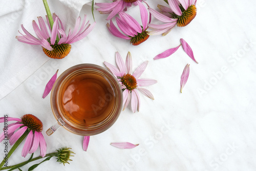 A cup of herbal tea with fresh echinacea flowers on a light table. Top view, flat lay. Spce for text. 