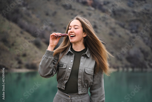 Fotografie Young cheerful hiker girl eating protein granola bar snack during vacation in na