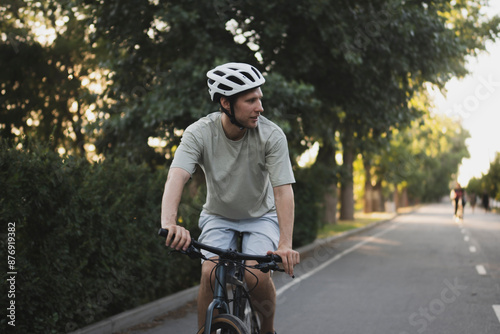 athlete man in a helmet rides a road bike down a paved path in a park, during the day © Mihail