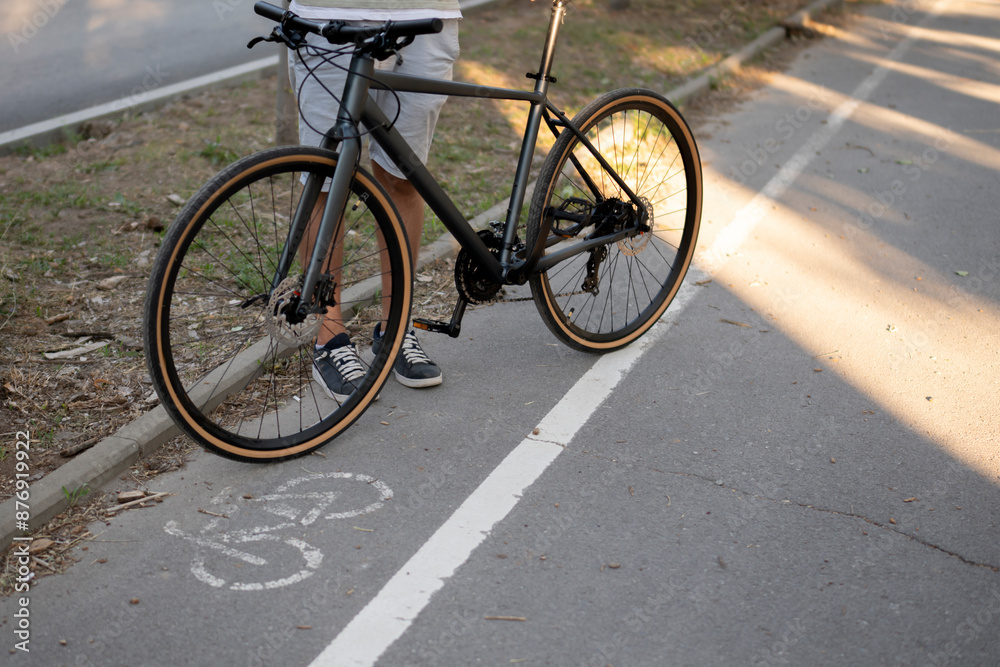 A person stands beside their bicycle on a bike path, with a white line separating the path from the sidewalk. environmentally friendly transport concept A person stands beside their bicycle on a bike path, with a white line separating the path from the sidewalk. environmentally friendly transport concept